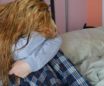 person with long hair sitting down with their head on their arms