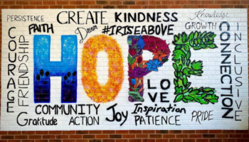 mural with a white backdrop; the word "hope" is in the center painted in color, surrounded by other positive words painted in black